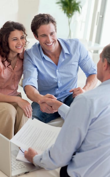 Un couple souriant serre la main d'un homme avec des documents et un ordinateur portable.
