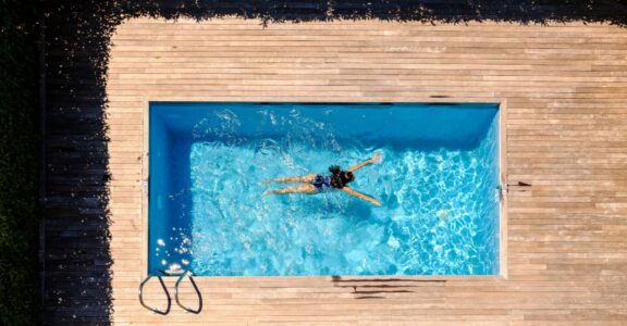 Une personne dans une piscine, terrasse en bois entourant.